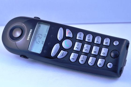 Black cordless landline handset with display and silver keypad on a light background
