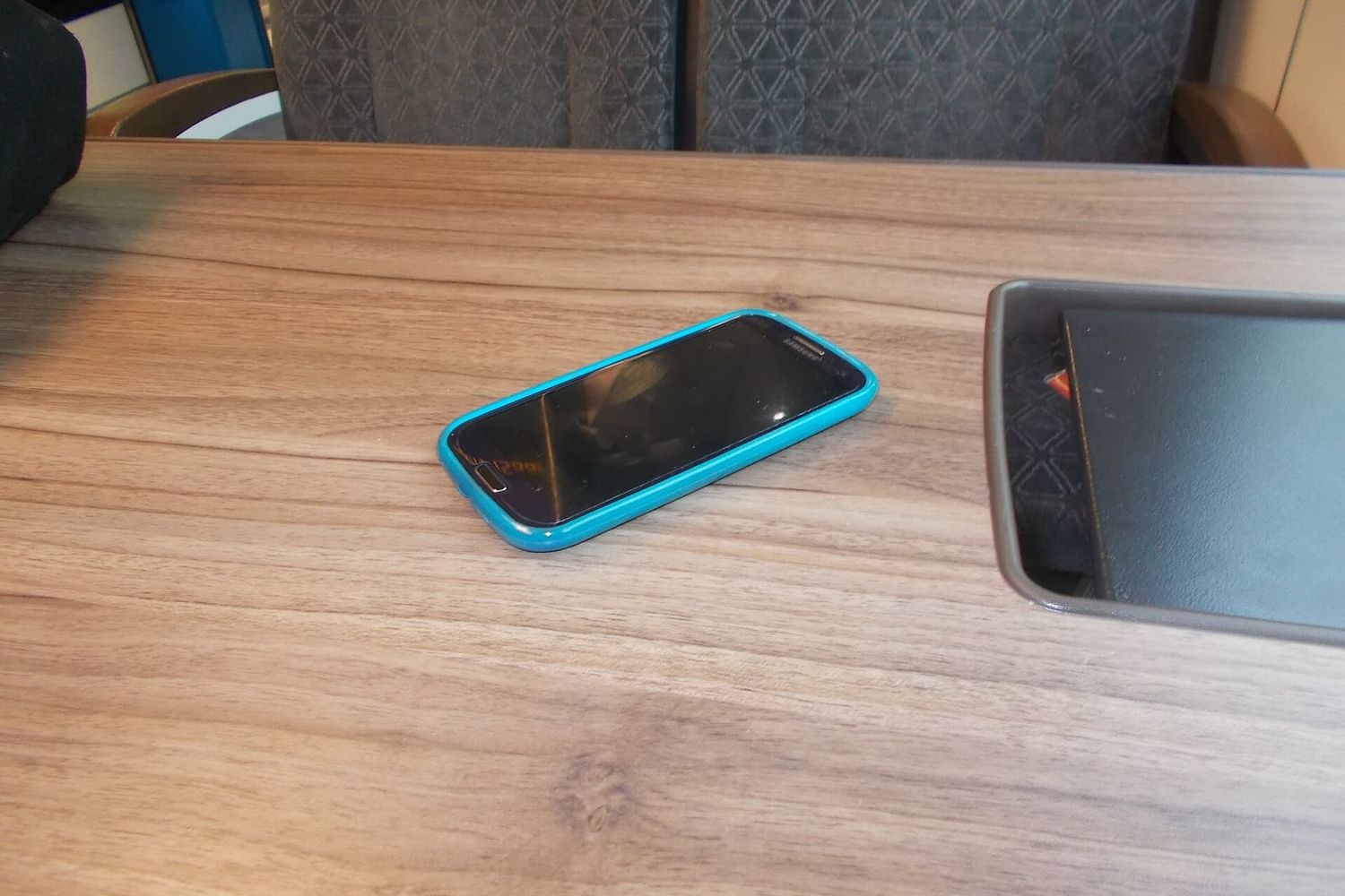 Smartphone with a dark screen in a turquoise case lying on a train table