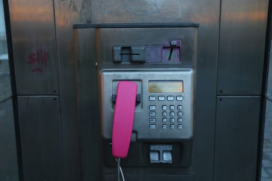 Public card payphone with a pink handset and metal keypad in a street phone booth