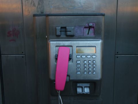 Öffentliches Kartentelefon mit pinkfarbenem Hörer und Tastenfeld in einer Telefonsäule