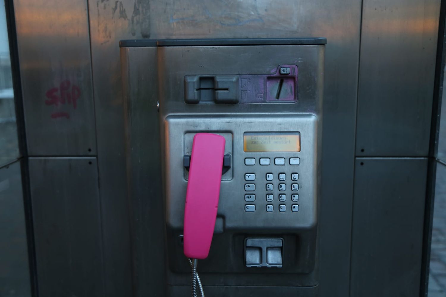 Öffentliches Kartentelefon mit pinkfarbenem Hörer und Tastenfeld in einer Telefonsäule