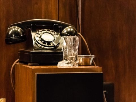 Black rotary telephone on a wooden cabinet next to two small glass boots