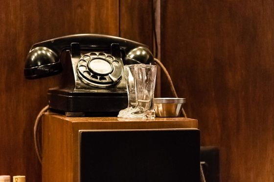 Black rotary telephone on a wooden cabinet next to two small glass boots
