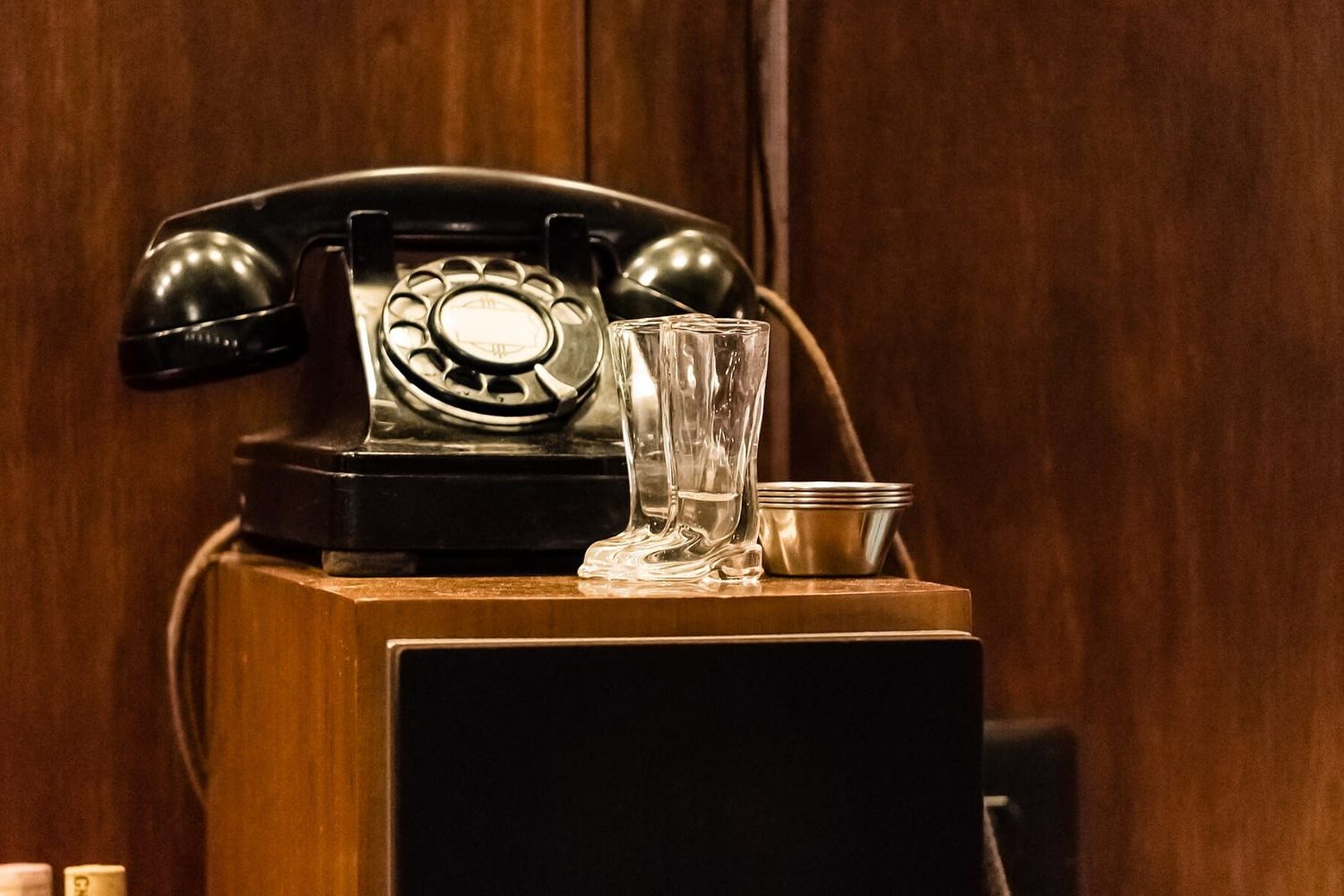 Black rotary telephone on a wooden cabinet next to two small glass boots